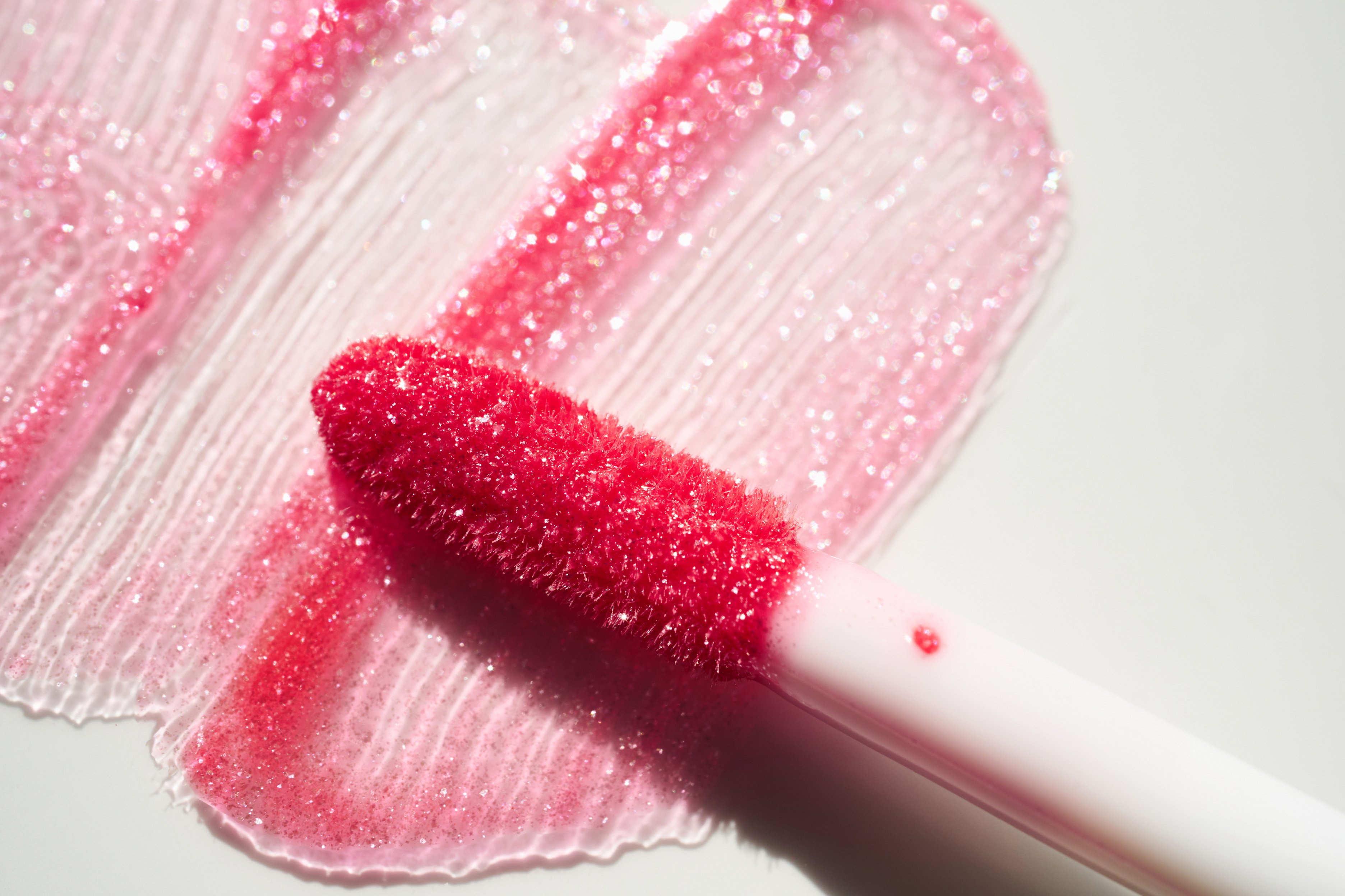 Smears of shining lip gloss and lip gloss brush on white background, hard shadows